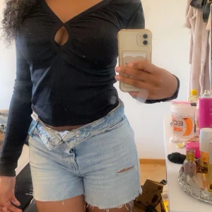 Svart ribbad topp från Gina Tricot - Svart långärmad topp från Gina Tricot med ribbad struktur och snygg v-ringning med twistad detalj och cut-out framtill. Modellen är croppad och sitter tight, perfekt till jeans eller kjol. Superenkel att styla för en trendig look.