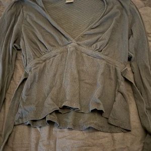 Svart knyt topp från Gina Tricot - Supersnygg svart knyt topp från Gina Tricot med v-ringning och lång ärm. Knytning i bak vilket framhäver midjan och allmänt en fin detalj.