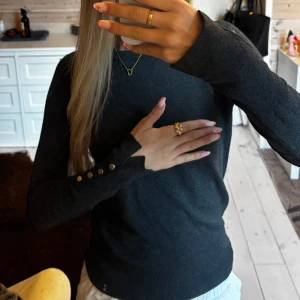 Svart stickad tröja från Zara - Svart stickad tröja från Zara med rund halsringning och långa ärmar. Ärmsluten har snygga guldfärgade knappar som detalj. Tröjan är enkel men stilren och passar perfekt till jeans eller kjol. Mjuk och skön känsla mot huden.