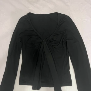 Svart långärmad topp med knyt SHEIN - Svart långärmad topp från SHEIN med snygg knytning framtill och djup v-ringning. Tillverkad i mjuk och stretchig polyesterblandning som sitter skönt på kroppen. Använd endast 1 gång. Orginal pris 120kr