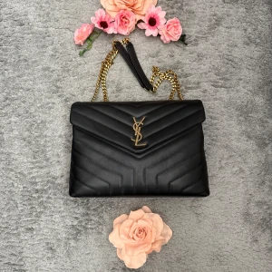 Svart quiltad YSL axelväska i skinn - Säljer en svart quiltad axelväska från YSL med ikoniskt guldigt YSL-emblem framtill. Väskan har kedjerem i guldmetall och är tillverkad i mjukt skinn. Snygg V-formad quiltning och klassisk kuvertform gör den till en riktig statement piece.Köpt här på Plick men passar inte mig så hoppas att någon annan vill ha den🥲💕🌺