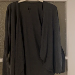 Mörkgrå lång kofta med långa ärmar - Säljer en enkel och stilren mörkgrå kofta med lång ärm. Koftan är öppen framtill och har en loose passform, perfekt att slänga på sig över en t-shirt eller topp. Passar både till jeans och kjol för en chill look.