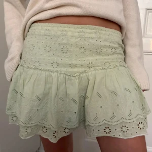 Ljusgrön broderad kortkjol - Supersöt ljusgrön kortkjol med broderade blommor och volangkant. Kjolen har elastisk midja och är gjord i tunn bomull, perfekt för varma dagar. Den har fina hålbroderier och en romantisk vibe som lyfter vilken outfit som helst.
