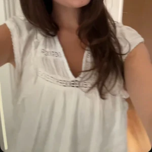 Vit blus med volang från Neo Noir - Supersöt vit blus från Neo Noir med volangdetaljer på axlarna och v-ringning. Blusen har broderade partier och är ärmlös med en luftig och flowy passform. Perfekt för en fräsch och somrig look. Nyköpt pris: 599 kr