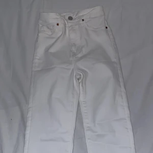 Vita högmidjade jeans med fransar  - Säljer ett par vita högmidjade tajta jeans med raka /bootcut ben och snygga fransar längst ner vid bensluten. Klassisk femficksmodell med knapp och dragkedja. Perfekta för dig som vill ha en clean och trendig look. 