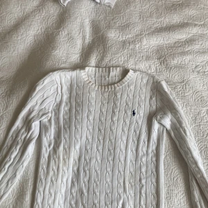 Vit tröja från Ralph Lauren - Vit kabelstickad tröja från Ralph Lauren med klassisk rund halsringning och broderad marinblå logga på bröstet. Tröjan har lång ärm och passar mig som har storlek S🫶🏼vid mer frågor kan du skriva till mig.
