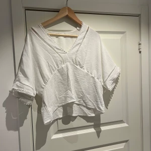 Vit blus med spets och v-ringning - Superfin vit blus med v-ringning och dekorativa spetsdetaljer längs halsringning och ärmslut. Blusen har korta, vida ärmar och en luftig, lite croppad passform. Perfekt för dig som gillar romantiska och boho-vibbar. Toppen är väldigt lik toppen från Zara men den är från SHEIN. Aldrig använd.
