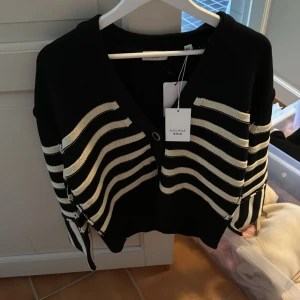 Svartvit randig kofta från Dagmar - Superfin oversized svart kofta från Dagmar med breda vita ränder och snygga knappar framtill. Koftan har v-ringning, lång ärm och är stickad i ett mjukt material. 