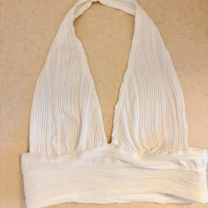 Vit halterneck tubtopp - Vit tubtopp med halterneck och djup v-ringning. Toppen har ett ribbat, veckat tyg. Köpt från Shein. Storlek: 38