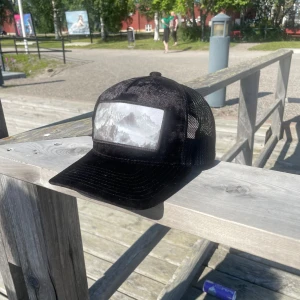 Svart keps från Hatstore med Hogwarts motiv - Svart keps från Hatstore med mesh på sidorna och böjd skärm. Framtill finns en stor patch med ett gråvitt motiv av hogwarts. Kepsen är tillverkad i polyester och har justerbar passform baktill. Perfekt för dig som gillar stilrena accessoarer med naturtema.