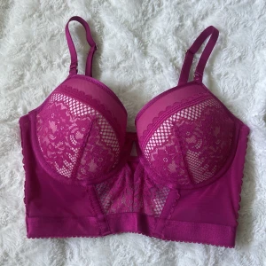Rosa spetskorsett/bh från Hunkemöller - Säljer en snygg rosa korsett/bh från Hunkemöller med vackra spetsdetaljer och justerbara axelband. Modellen har vadderade kupor, hakknäppning bak och meshpartier som ger en extra cool look. Perfekt för dig som vill ha något unikt och trendigt.
