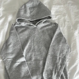 Grå hoodie från 157 med huva - En stilren grå hoodie från 157 med klassisk huva och stor magficka. Perfekt för chill dagar eller när du vill ha en enkel och snygg look. Mjuk insida och ribbade muddar för extra komfort.