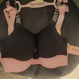 Juicy Couture svart och rosa linnetopp - Två snygga linnetoppar från Juicy Couture, en i svart och en i ljusrosa. Båda har breda axelband med logotypen tryckt i vitt och rosa. Perfekta för att ge en sportig och trendig vibe till din outfit.