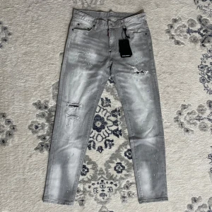 Dsquared2 jeans - Snygga grå jeans från Dsquared2 med slitningar, färgstänk och coolt tvättad look. Klassisk femficksmodell med Dsquared2-logga på både etikett och bakficka. Perfekta för dig som gillar streetstyle och vill sticka ut.