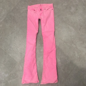 Rosa bootcut jeans med slits - Säljer ett par riktigt snygga rosa jeans med bootcut-modell och slitna slitsar nertill. Byxorna har klassisk femficksdesign och låg midja. Perfekta för dig som vill sticka ut med färg och coola detaljer. Materialet är mjukt och skönt bomullstyg. Dem är små i storlek 