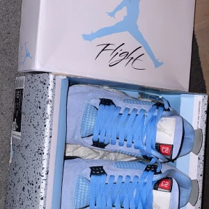 Nike Air Jordan 4 University Blue - Nike Air Jordan 4 Retro i färgen University Blue. Skorna har ljusblå mocka, svarta och grå detaljer samt den klassiska Jumpman-loggan på hälen. Snygga blå skosnören och röd 23-detalj på plösen. Perfekta för dig som vill sticka ut med en ikonisk sneaker. Storlek 44, nya med orginal box. 