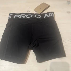 Svarta Nike Pro träningstights-shorts - Svarta tighta träningstights-shorts från Nike Pro med bred resår i midjan och logga i vitt. Snygg sportig look, perfekt för gymmet eller löpning. Materialet är stretchigt och följsamt för maximal rörelsefrihet. Aldrig använda. Det är storlek M i kids.