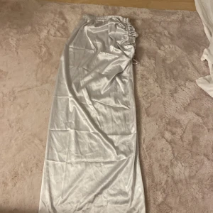 Satin kjol  från Femme Luxe - Snygga vida byxor i glansigt silverfärgat satin från Femme Luxe. Byxorna har resår i midjan och coola snörningsdetaljer längs ena sidan som ger en unik look. Perfekta för dig som vill sticka ut med en trendig och lyxig vibe.