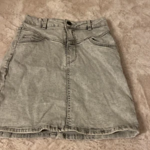 Grå jeanskjol från Bershka - Säljer en grå jeanskjol från Bershka i klassisk femficksmodell. Kjolen är kort, har bälteshällor och dragkedja med knapp framtill. Perfekt för dig som gillar en enkel och stilren look med denimkänsla.