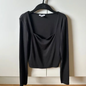 Svart långärmad topp från Amisu - Svart långärmad topp från Amisu med snygg fyrkantig ringning och lätt drapering framtill. Modellen är croppad och sitter tajt mot kroppen, perfekt att styla med höga jeans eller kjol. Mjuk och stretchig känsla.