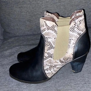 Chelsea boots med ormskinnsmönster - Snygga chelsea boots i svart skinn med coola detaljer i beige och brunt ormskinnsmönster. Rund tå och stabil klack ger både stil och komfort. Perfekta för dig som vill sticka ut med dina skor.