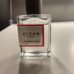 CLEAN Classic Strawberry Fields parfym - Luktar supergott!!! Fräsch parfym från CLEAN Classic i doften Strawberry Fields. Flaskan är fyrkantig i genomskinligt glas med en enkel vit etikett och röd ram. Parfymen har en metallfärgad spraykork och en stilren, minimalistisk design som passar perfekt på sminkbordet.