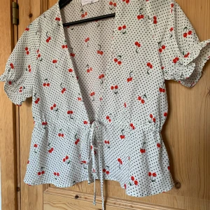 Söt blus med körsbär - Supergullig blus med körsbär i svalt material, perfekt till sommaren. Har knytning i midjan så skulle säga att den passar XS-S. Jättefint skick! Längd 51cm