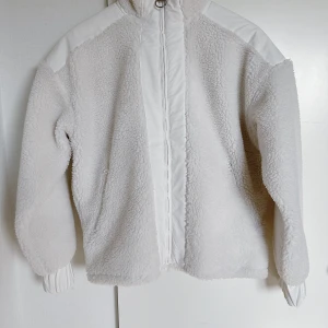 Vit teddyjacka från Peak Performance - Säljer en superfin och mysig Peak Performance pufferjacka i teddy fleece, perfekt för vår, höst och vinter. Färgen är en stilren offwhite med snygga kontrastdetaljer. Använd endast 2 gånger, så den är i mycket bra skick! Storlek Small (S), passar true to size.  Jackan har en hög krage, dragkedja med ringdetalj, elastiska ärmslut och två praktiska fickor med dragkedja. Varm men ändå lätt och bekväm.  Perfekt för dig som gillar streetwear, skandinavisk minimalism eller letar efter en trendig teddy