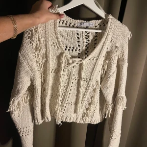 Vit stickad tröja från Zara - Säljer en vit stickad tröja från Zara med fransiga detaljer och ett öppet stickmönster. Tröjan är croppad och har långa ärmar. Säljs inte längre! 