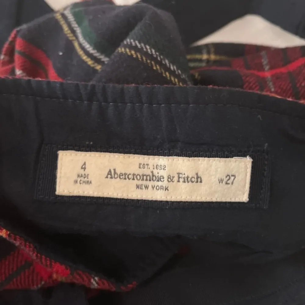 Snygg rutig kjol från Abercrombie & Fitch i rött och svart med en söt rosett framtill. Kjolen har ett klassiskt rutmönster och en liten älgbroderi i nederkanten. Perfekt för en stilren look!. Hameet.