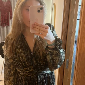 Glittrig klänning med omlott - Säljer en glittrig klänning i mörka toner med omlott-design och långa ärmar. Perfekt för en kväll ute eller en speciell tillställning. Klänningen har en v-ringad hals och ett elegant fall.