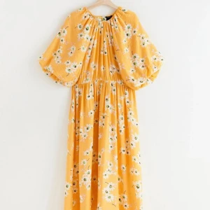 Gul blommig klänning från Lindex strl M - Charmig gul klänning med blommigt mönster. Den har korta ärmar och en lös passform som ger en avslappnad känsla. Perfekt för soliga dagar och sommarens äventyr.