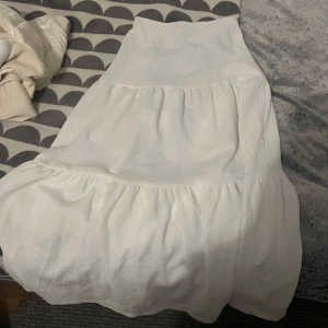 Vit kjol från Gina Tricot - Säljer en vit kjol från Gina Tricot med en luftig och bekväm passform. Kjolen har en volangdesign som ger den ett fint fall. Perfekt för varma dagar och kan enkelt matchas med olika toppar.