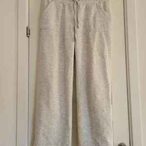 Grå mjukisbyxor med dragsko - Bekväma grå mjukisbyxor med elastisk midja och dragsko. Byxorna har en loose passform och är perfekta för en avslappnad stil. Tillverkade i mjukt material för extra komfort och har även fickor därbak. 