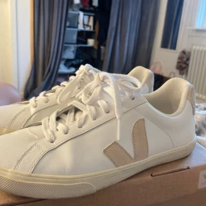 Veja skor - Snygga vita sneakers från Veja med beige detaljer och snörning. Tillverkade i skinn med en stilren design som passar perfekt till vardags. Märket Veja syns tydligt på hälen och sidan av skorna.Pris kan diskuteras vid snabb affär!Väldigt väldigt fina, säljer då de är lite förstora för mig och har därför bara använt de ca 3 gånger! Det lite ”gråa” på märkena bak som man ser på bild 2 för att mina jeans färgade av sig. Det kan gå att fixa med rätt medel, men är inget man tänker på 