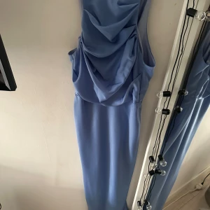 Ljusblå långklänning med drapering -  ljusblå långklänning med draperad detalj framtill. Klänningen är ärmlös och den har en dragkedja baktill. Endast använd en kväll och inga defekter på! Säljer den gärna då den inte kommer till användning😊