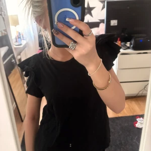 Svart topp med volangärmar - Säljer en stilren svart topp med volangdetaljer på ärmarna.