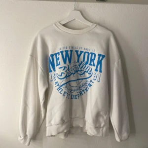 Vit sweatshirt med blå text - Säljer en vit sweatshirt med blå text 'New York Brooklyn Athletic Department' tryckt på framsidan. Ska flytta snart så vill gärna bli av med allt så fort som möjligt (pris kan diskuteras)💕