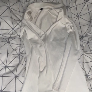 Vit ribbad klänning H&M - Säljer en stilren vit ribbad klänning från H&M med dragkedja framtill. Klänningen har långa ärmar och en figurnära passform som ger en snygg siluett. 