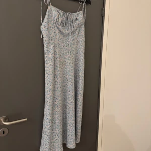 Blommig klänning från Adoore - Söt blommig klänning från Adoore aldrig använd i ljusblått med små blommor i rosa och vitt. Klänningen har smala axelband och en knytning framtill. Storlek 38 men går att justera med banden till 36! Går gärna ner i pris vid snabb affär🥰