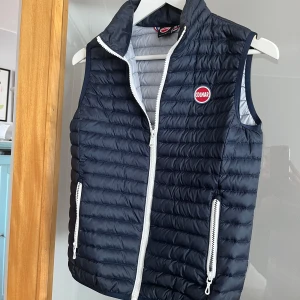 Mörkblå dunväst från Colmar stl 12 År  - Snygg mörkblå dunväst från Colmar med vit dragkedja och logga på bröstet. Perfekt för kyligare dagar. Västen har en quiltad design och två praktiska fickor med dragkedja.