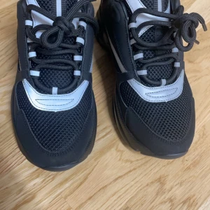 Svarta sneakers Dior b22s - Snygga svarta sneakers från Dior med reflekterande detaljer och snörning. Tillverkade i Italien, dessa skor kombinerar stil och komfort perfekt. Perfekta för dig som vill ha en exklusiv look.