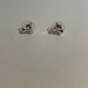 Söta rosettformade örhängen i silver - Charmiga små örhängen i form av rosetter, tillverkade i silver. Perfekta för att ge en subtil och elegant touch till din stil. Passar bra till både vardag och speciella tillfällen.