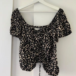 Leopardmönstrad topp - Supersöt leopardmönstrad topp med korta ärmar och smockdetaljer. Toppen har en knytning framtill och ger en bra passform! 