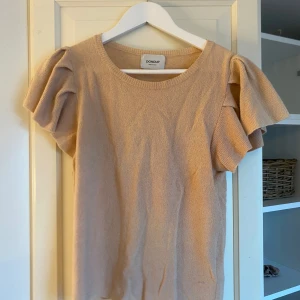 Beige topp från Dondup - Säljer en stilren beige topp från Dondup med korta ärmar och volangdetaljer. Toppen har en rund halsringning och är tillverkad i ett mjukt material.