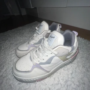 Vita sneakers från Axel Arigato - Snygga vita sneakers från Axel Arigato med pastellfärgade detaljer i rosa och beige. Skorna har en chunky sula och snörning framtill. Perfekta för en trendig look.