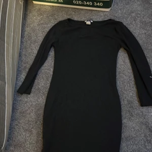 Mörkgrå klänning från Basic H&M - Snygg svart klänning från H&M i en enkel och stilren design. Klänningen har långa ärmar och en figurnära passform som passar perfekt för olika tillfällen. Ett måste i garderoben för den som gillar klassiska plagg.