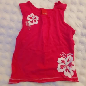 Skrikrosa  klänning från Esprit - Säljer en söt klänning från Esprit med vita blommor tryckta på framsidan. Perfekt för varma dagar och ger en härlig sommarkänsla. Klänning i storlek 74 för små barn.