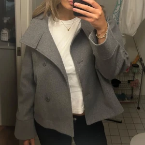 Grå kappa från Gina Tricot  - Snygg grå kappa från Gina Tricot med hög krage och knappar framtill. Jackan har en stilren design med långa ärmar och en rak passform. Perfekt för kyligare dagar. Jackan är använd några gånger men är i ett mycket bra skick. ‼️OBS inte mina bilder‼️