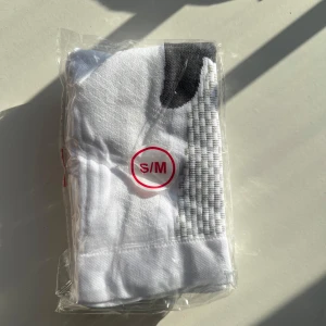 Vita strumpor i storlek S/M - Säljer ett par vita strumpor i storlek S/M. De är förpackade i plast och har en grå detalj vid hälen. Perfekta för vardagsbruk eller träning.Stödstrumpor är en enkel men effektiv lösning för att förbättra blodcirkulationen och minska svullnad i benen. De är perfekta för långa arbetsdagar, resor eller för den som lider av trötta och tunga ben. Genom att ge ett lätt tryck på benen hjälper de till att förebygga problem som åderbråck och förbättra återhämtningen efter träning. Investera i stödstrump